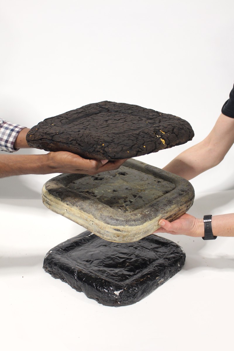 Three hands stacking square slabs of pressed coffee grounds in three shades