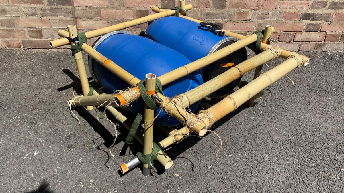 Bamboo frame holding two blue plastic barrels, joined with green nylon straps, screws and jute rope